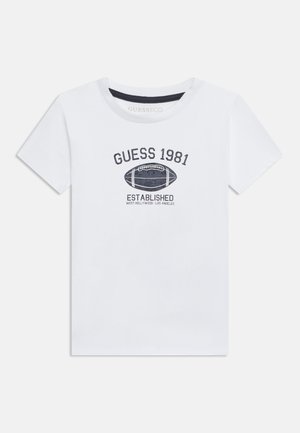 Hvid kortærmet t-shirt med sort tekst "GUESS 1981" over en fodboldgrafik og "ESTABLISHED WEST HOLLYWOOD LOS ANGELES" under.