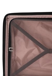 Otevřený kufr s světlou růžovou podšívkou, síťovanou zipovou kapsou a černými křížovými elastickými popruhy pro upevnění obsahu.