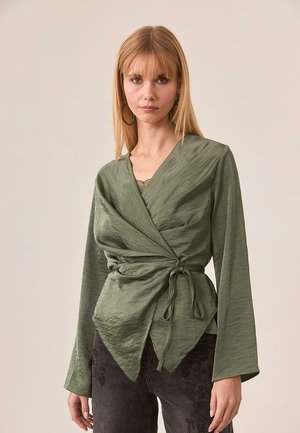 Top envolvente de color verde oliva con mangas largas, tejido texturizado y cintura anudada. Escote en V profundo y silueta relajada destacados.