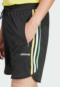 Svarta nät-träningsshorts med dragsko i midjan, som har gröna, gula och vita sidstreck, samt en dragkedjefick på sidan.