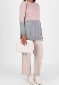 Maglione a maglia di un rosa chiaro e grigio con texture a coste, abbinato a pantaloni beige a gamba larga e una borsa a tracolla trapuntata color crema. Stivaletti con tacco completano il look.