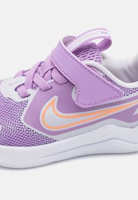 Chaussure de sport violette avec une tige en mesh, des accents synthétiques et une semelle blanche. Comprend des lacets et une sangle Velcro pour un ajustement sécurisé.