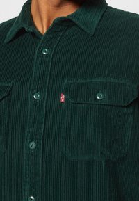 Camicia in velluto a coste verde con superficie strutturata, dotata di colletto con bottoni, tasche frontali e un piccolo logo rosso di Levi's.