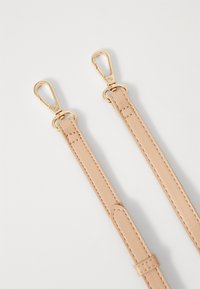 Beige leather strap with two golden clips, featuring stitching details and a smooth texture, designed for versatility in use.