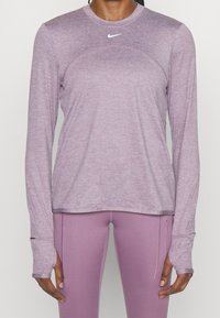 Person iført en lyse lilla langærmet træningstrøje og matchende tætsiddende leggings med hul til tommelfingrene og en lille lynlåslomme på låret.