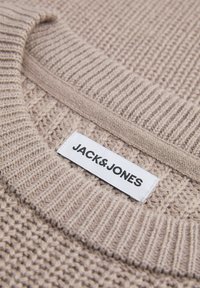 Beige gestrickter Pullover mit gerippter Textur, Rundhalsausschnitt und einem weißen Etikett mit der Aufschrift "JACK & JONES" in schwarzem Text.