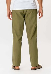 Olivengrønne, letvægtsbukser med en løstsiddende pasform. Har en glat tekstur og lige snit, parret med brune sandaler.