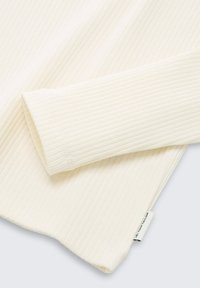 Geribbelde longsleeve top in off-white, met een zachte textuur, opgerolde manchetten en een klein merklabel aan de zoom.