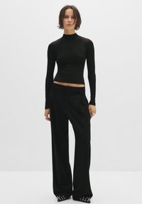Czarny longsleeve top z golfem w dopasowanym kroju, połączony z czarnymi spodniami z szerokimi nogawkami, charakteryzującymi się gładką teksturą i ozdobnymi detalami na butach.