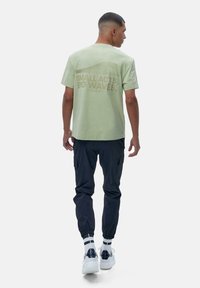 Lysegrønn bomullst-skjorte med grafisk tekst på ryggen. Kombinert med svarte cargosbukser og hvite sneakers med marineblå detaljer.