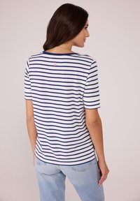 Gestreiftes T-Shirt mit marineblauen und weißen horizontalen Streifen, rundem Ausschnitt, kurzen Ärmeln und einem kleinen pinken Herzdettail auf dem Rücken.