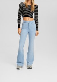 Jeans acampanados de un azul claro, hechos de denim, de talle alto con un desvanecimiento sutil. Combinados con una blusa de manga larga recortada a rayas en blanco y negro.