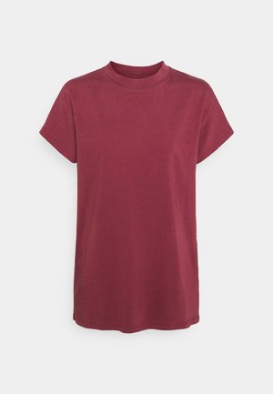 Kortærmet, rundhalset, løs, ensfarvet T-shirt i mørkerød på en ensfarvet lys baggrund.