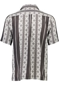 Camisa de manga corta en blanco y marrón oscuro, con un patrón geométrico de rayas y acentos en contraste. Tela ligera y tejida.