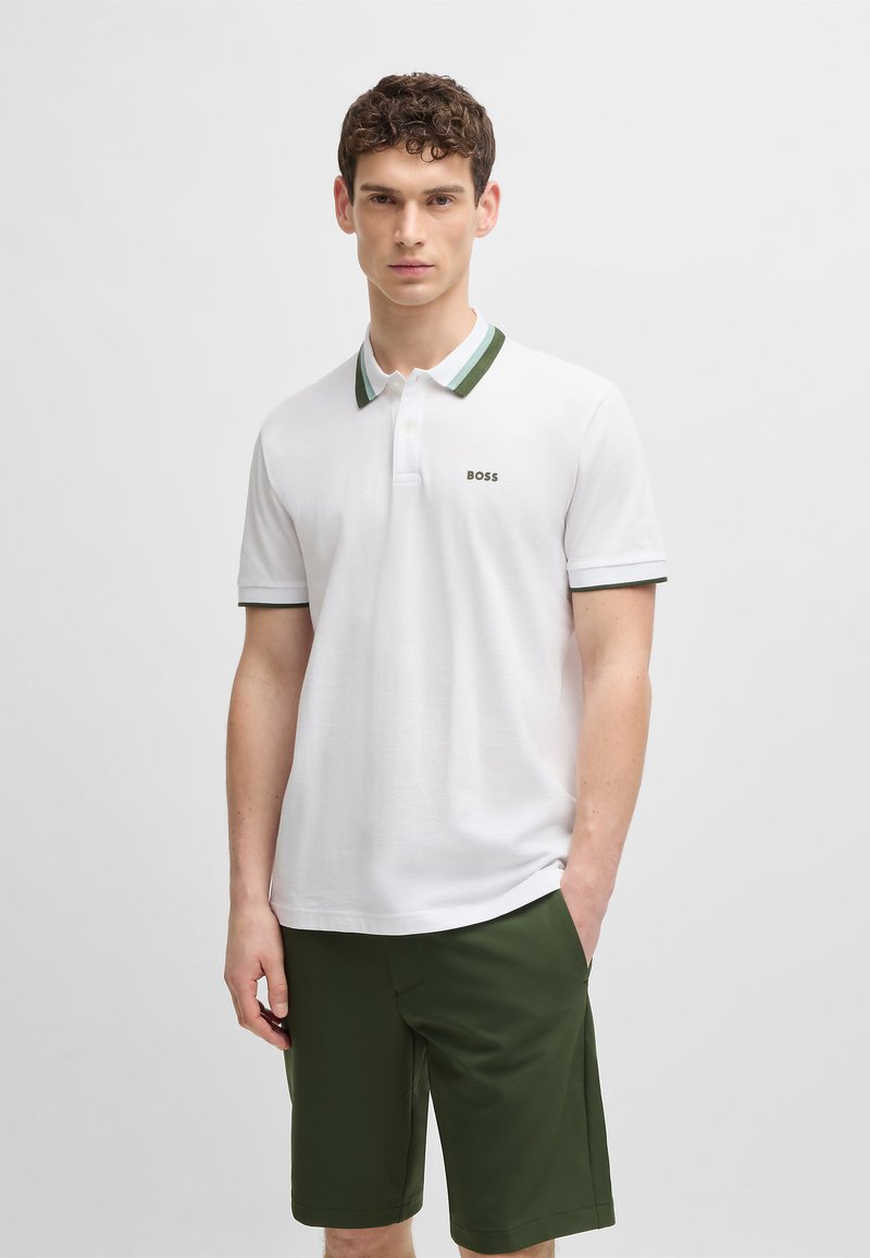 White polo shirt with green and white striped collar, featuring a subtle "BOSS" logo. Worn with dark green shorts.
