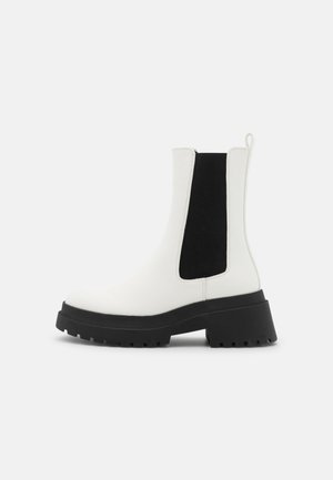 Hvid Chelsea-støvle til midtkalv med sort elastisk sidepanel, tyk sort kraftig sål og trækflig på en ensartet lys baggrund.