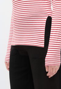 Piros-fehér csíkos hosszú ujjú ing oldalsó sliccel, fekete nadrággal párosítva. Az ing puha textúrájú és kényelmes, bő szabású.