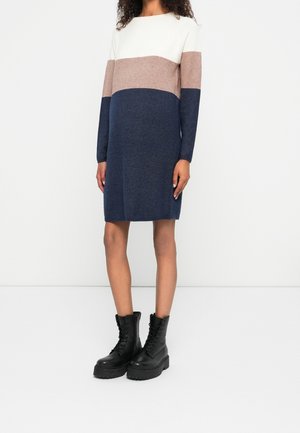 Knit dress featuring a color-block design with white, light brown, and navy sections. Long sleeves and a straight silhouette. Worn with black leather boots.