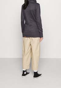 Felpa a maniche lunghe grigia scura con colletto alto, abbinata a pantaloni beige larghi e sneakers nere con dettagli bianchi.
