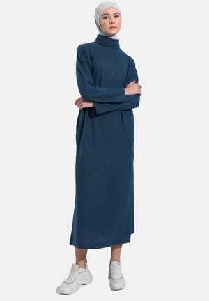 Long, dark blue turtleneck dress with long sleeves, made from soft fabric; worn with white sneakers. Smooth texture, minimal design.