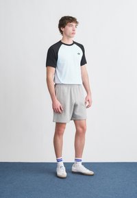 Λευκό και μαύρο κοντομάνικο μπλουζάκι, γκρι αθλητικά σορτς, λευκά αθλητικά παπούτσια με μπεζ σόλες και κάλτσες με μπλε ρίγες. Απλός σχεδιασμός, άνετη εφαρμογή.