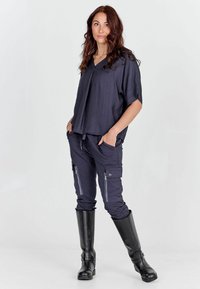 Voľné, tmavosivé tričko s krátkymi rukávmi, skombinované s tmavými cargo nohavicami s vreckami na zips a čiernymi čižmami po kolená.