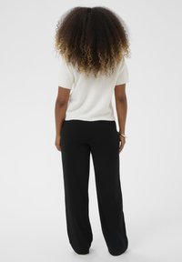 Top alb cu mânecă scurtă, asortat cu pantaloni largi negri. Topul are un tricot texturat, în timp ce pantalonii au o finisare netedă a stofei.