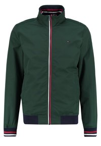 Tmavě zelená bunda na zip s vysokým límcem, žebrovanými manžetami a lemem s červenými, bílými a námořnickými pruhy a malým logem na levé straně hrudi.