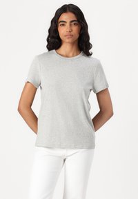 Tricou scurt cu maneci dintr-un material moale, de culoare gri deschis. Are un decolteu rotund și o croială lejeră, asociat cu pantaloni albi.
