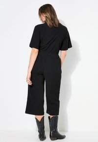 Mono negro de manga corta y piernas anchas, ceñido a la cintura. Combinado con botas vaqueras negras con un patrón texturizado.