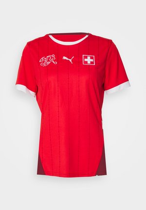 Maglia sportiva rossa con colletto e bordi delle maniche bianchi, caratterizzata dalla bandiera svizzera, dal logo Puma e dallo stemma della federazione svizzera di hockey su campo.