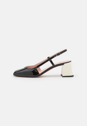Chaussure femme slingback en cuir verni noir, bout pointu, bride réglable et talon bloc blanc épais.