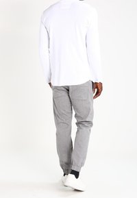 Chemise blanche à manches longues avec un ourlet arrondi, associée à un pantalon gris fuselé avec un poignet élastique. Les chaussures sont blanches avec peu de détails.