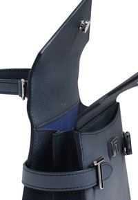 Marineblaue Lederhandtasche mit strukturierter Oberfläche, ausgestattet mit einem silbernen Druckknopfverschluss und einem kontrastierenden blauen Innenraum. Verstellbarer Tragegurt sichtbar.