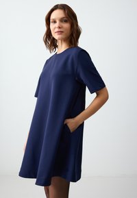 Abito blu navy a maniche corte con una vestibilità ampia, dotato di tasche laterali e scollatura rotonda. Tessuto morbido con cuciture minime.