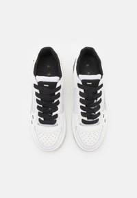 White sneakers with black laces, textured synthetic upper, perforated toe, and subtle grey accents. Cushioned interior and flat sole.