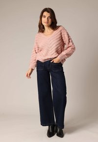 Pull en tricot rose clair avec un col en V et une texture en zigzag, associé à un jean large bleu foncé et des bottines noires.