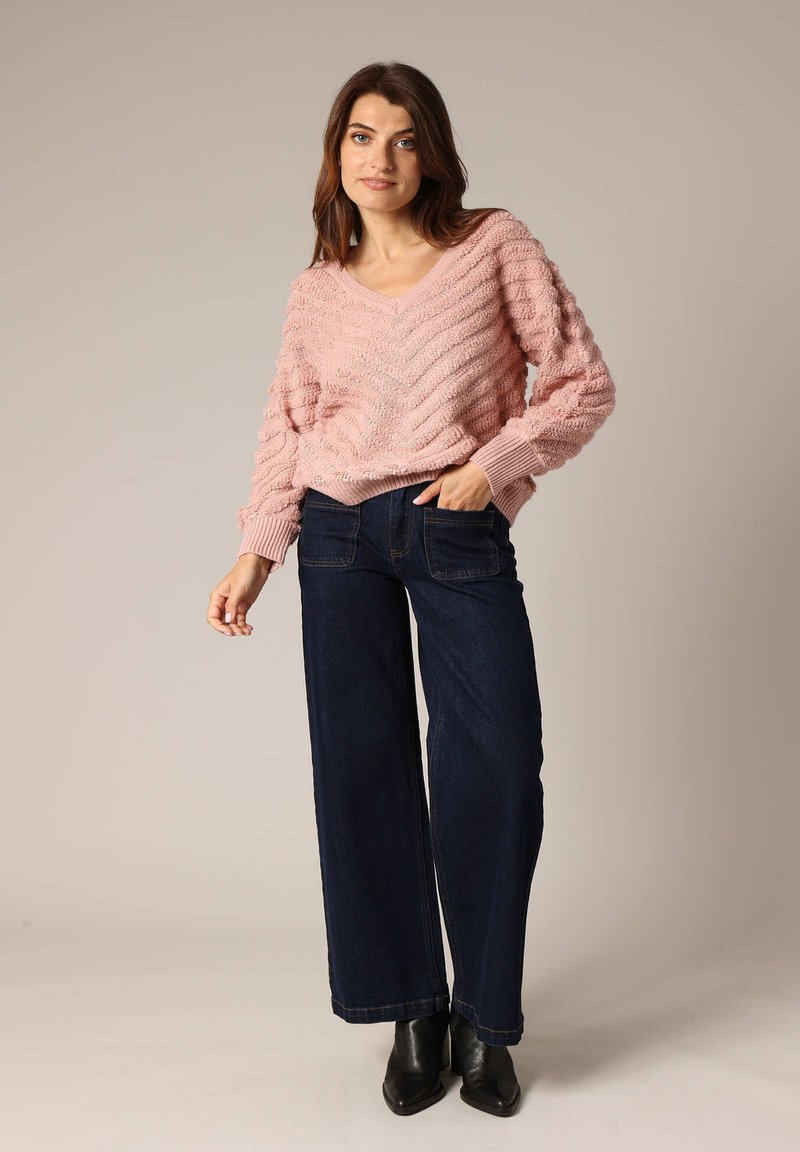 Pull en tricot rose clair avec un col en V et une texture en zigzag, associé à un jean large bleu foncé et des bottines noires.