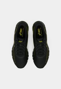 Ζευγάρι μαυρόκ Yellow Asics Gel-Quantum 360 αθλητικά παπούτσια με κορδόνια, από πάνω σε λευκό φόντο.