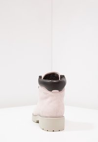 Bota de tobillo de ante rosa con un collar de cuero negro, superficie texturizada y una gruesa suela de goma blanca. La vista trasera muestra una forma redondeada.