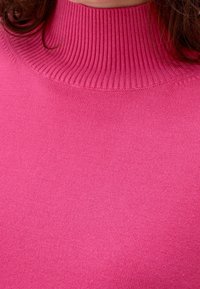 Eng anliegender rosa Pullover mit hohem, geripptem Kragen. Weiche Textur und glatte Oberfläche. Der Stoff ist einheitlich gefärbt ohne sichtbare Muster oder Verzierungen.
