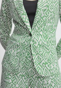 Green and white patterned suit, featuring a fitted blazer with a notch lapel and a matching pant. The texture is smooth with subtle detailing.