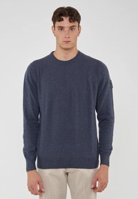 Maglione blu scuro realizzato in materiale morbido, con scollo rotondo e maniche lunghe. Include un piccolo logo sulla spalla sinistra.