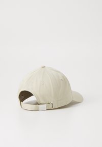 Cappellino da baseball in cotone beige con visiera curva, chiusura con cinturino regolabile e un accento metallico sul retro. Tessuto testurizzato con dettagli di cucitura.