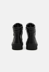 Černé kotníkové boty vyrobené z syntetické kůže, s uzavíráním na zip a silnou, drsnou podešví pro podporu. Hladký povrch bez vzorů.