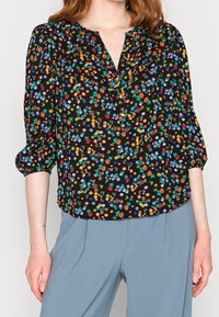 Blouse noire à motif floral multicolore, dotée d'un décolleté en V et de manches bouffantes trois-quarts. Tissu lisse à la texture douce.