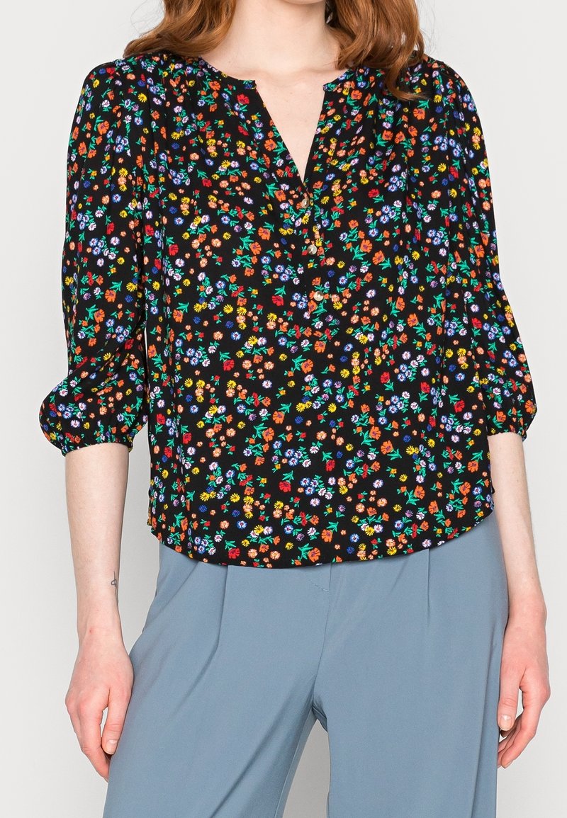 Blouse noire à motif floral multicolore, dotée d'un décolleté en V et de manches bouffantes trois-quarts. Tissu lisse à la texture douce.