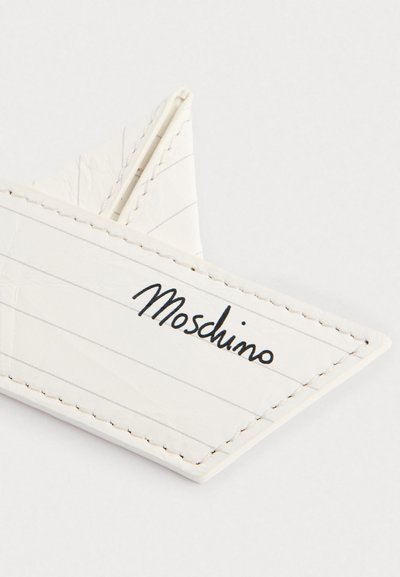 Biały skórzany portfel na karty z ukośnymi przeszyciami i niebieskimi liniami, z logo "Moschino" w czarnym kursywie.