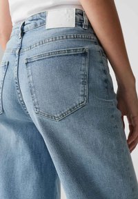 Light blue denim jeans with a straight leg design, featuring two back pockets and a white brand label at the waistband.