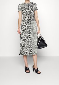 Sukienka midi w kwiatowy wzór w czerni i bieli, z krótkimi rękawami i okrągłym dekoltem. Uzupełniona czarną torebką i czarnymi sandałami na obcasie.